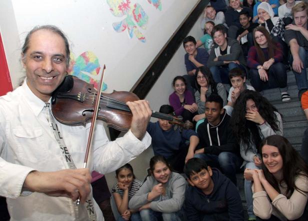Ein Mann spielt Geige vor einer Gruppe von Schülern auf einer Treppe.