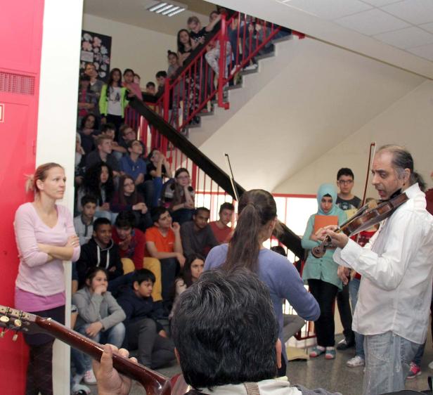 Ein Mann spielt Geige vor einer Gruppe von Schülern auf einer Treppe.