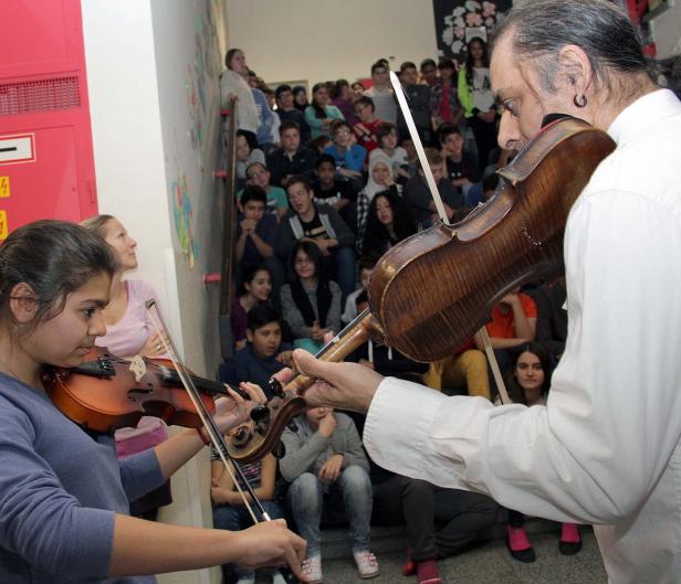 Eine junge Frau und ein Mann spielen Geige vor einer Gruppe von Schülern auf einer Treppe.
