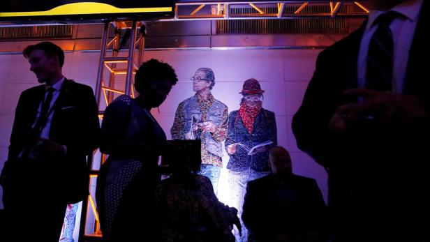 Menschen stehen vor einem beleuchteten Hintergrund mit zwei Figuren im Mosaikstil.