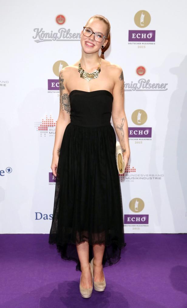 Eine junge Frau mit Brille und Tätowierungen in einem schwarzen Kleid auf dem roten Teppich der Echo-Verleihung.