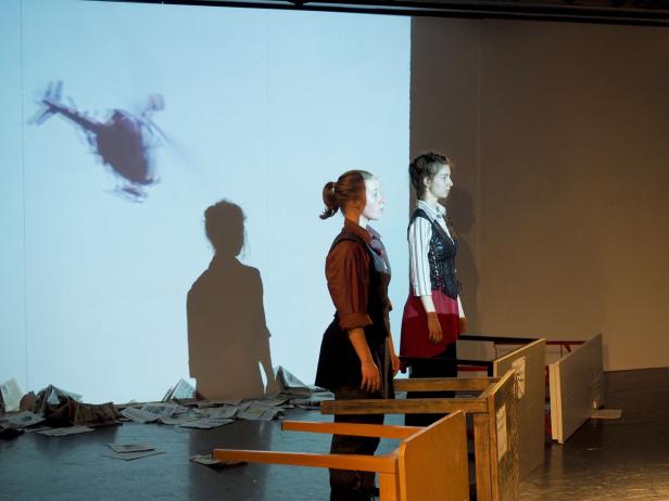 Zwei Frauen stehen auf einer Bühne vor einer Projektion eines Hubschraubers.