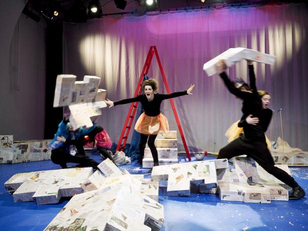 Eine Theaterszene mit Schauspielern und Requisiten aus Zeitungspapier auf einer Bühne.
