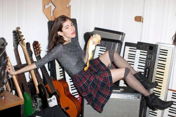 Eine Frau sitzt inmitten von Gitarren und Keyboards und schält eine Orange.