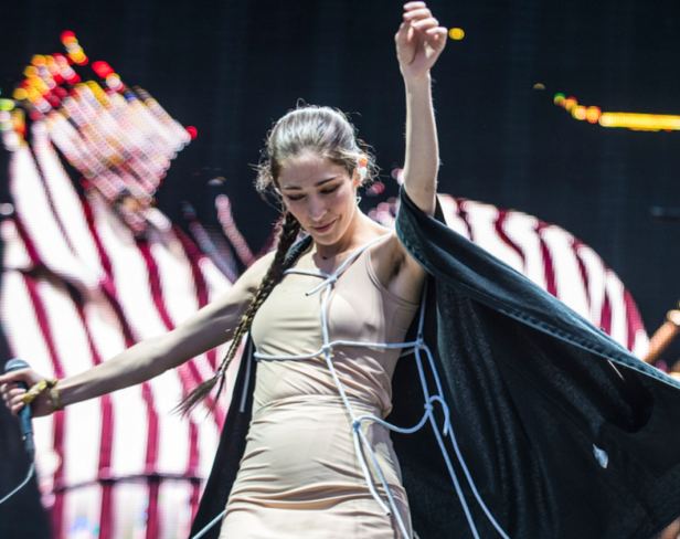 Eine Sängerin mit Zöpfen und einem beigen Kleid steht auf der Bühne und singt.