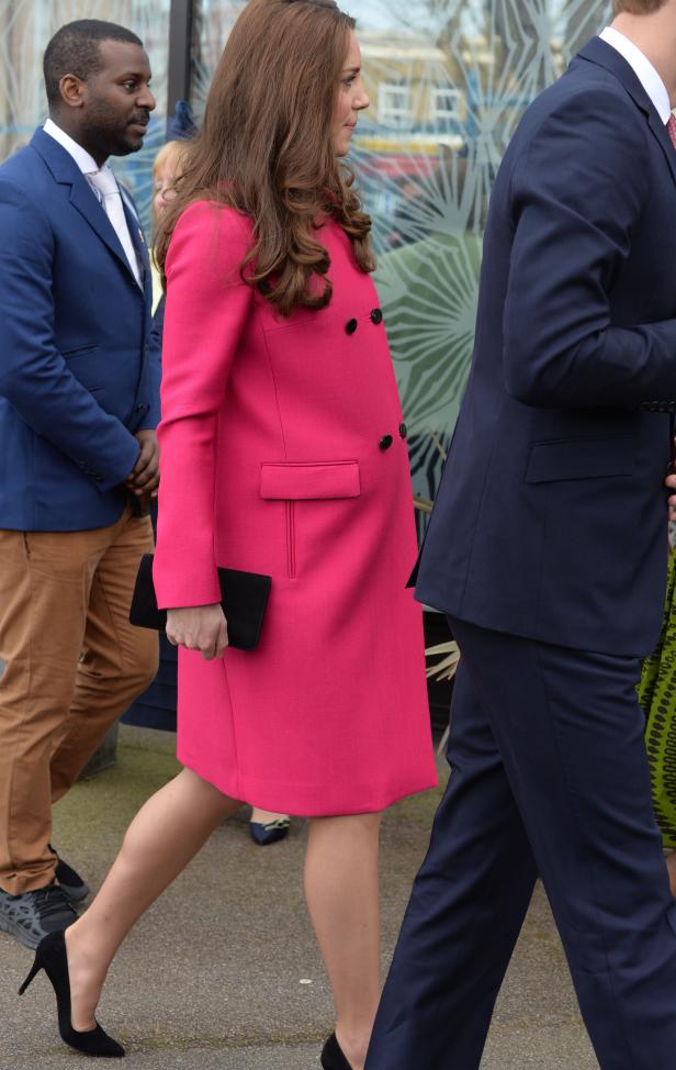 Kate Middleton in einem pinkfarbenen Mantel mit schwarzer Clutch und High Heels.