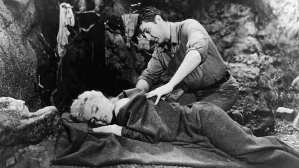 Marilyn Monroe im Film 'River of No Return' Szene mit Marilyn Monroe, die auf einer Decke liegt, während ein Mann sich um sie kümmert.