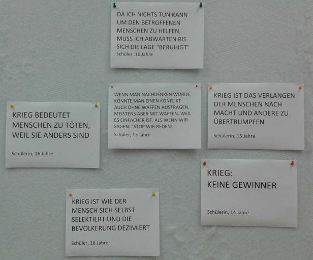 Mehrere Zettel mit Aussagen von Schülern zum Thema Krieg hängen an einer Wand.