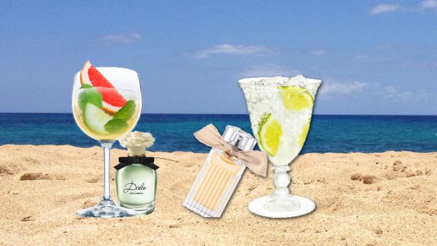 Zwei Parfümflaschen und zwei Cocktails stehen am Strand.