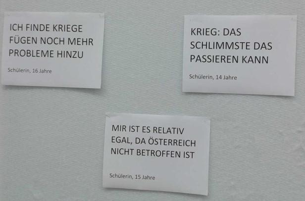 Drei Zettel mit Aussagen von Schülerinnen zum Thema Krieg hängen an einer Wand.