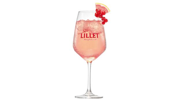 Ein Glas Lillet mit Eiswürfeln, Johannisbeeren und einer Zitronenscheibe auf weißem Hintergrund.
