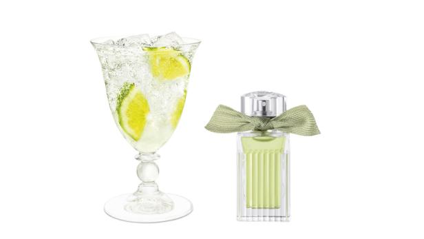 Ein Glas mit einem Getränk mit Limetten und Eiswürfeln neben einem Parfüm mit Schleife.