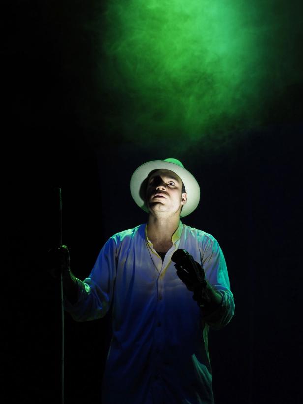 Ein Mann mit Hut und Handschuhen steht im Scheinwerferlicht.