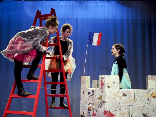 Drei Schauspielerinnen auf einer Bühne mit einer roten Leiter und einer französischen Flagge.