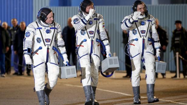 Drei Astronauten in Raumanzügen gehen mit kleinen grauen Boxen in der Hand.