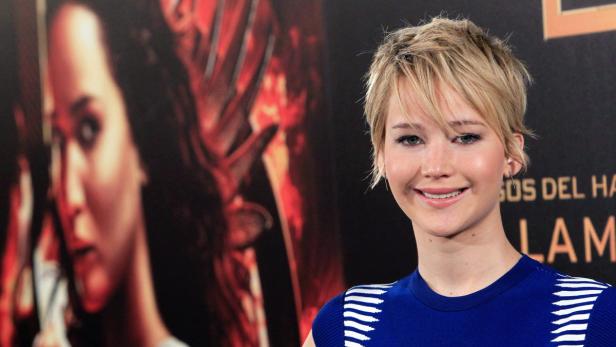 Jennifer Lawrence lächelt vor einem Poster für „Die Tribute von Panem – Mockingjay Teil 1“.