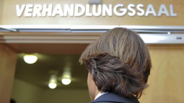 Eine Person steht vor einem Schild mit der Aufschrift „Verhandlungssaal“.