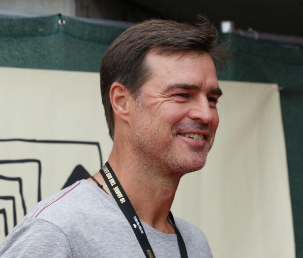 Ein lächelnder Mann mit grau meliertem Haar trägt ein graues T-Shirt.