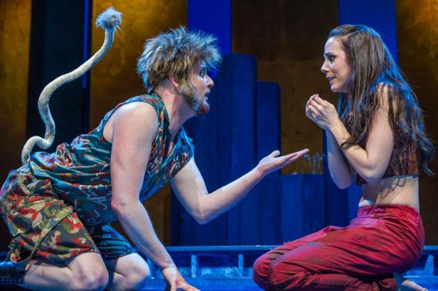 Ein Mann mit einem Affenschwanz kniet vor einer Frau auf einer Bühne.