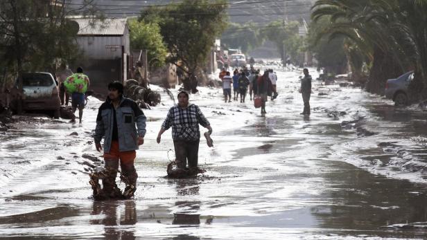 Menschen waten durch eine überflutete Straße nach einem Unwetter.