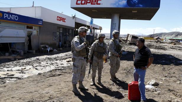 Soldaten stehen vor einer zerstörten COPEC-Tankstelle und sprechen mit einem Mann.