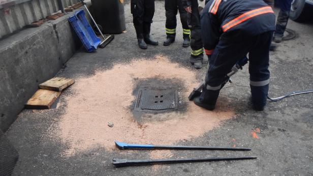 Arbeiter öffnen einen Kanaldeckel mit Werkzeugen und Sand.