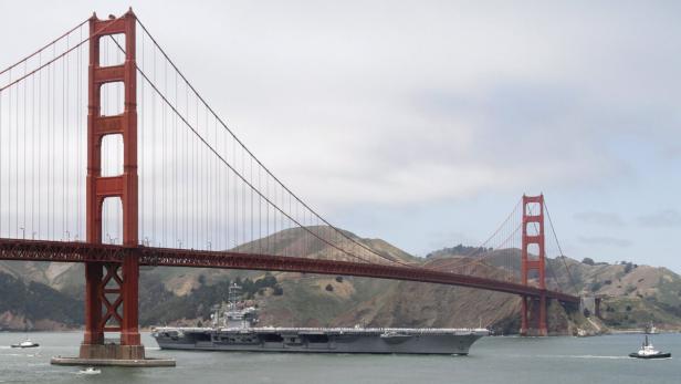 Ein Flugzeugträger fährt unter der Golden Gate Bridge hindurch.