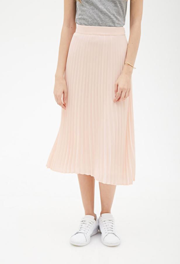 Eine Frau trägt einen hellrosa Faltenrock und weiße Turnschuhe.