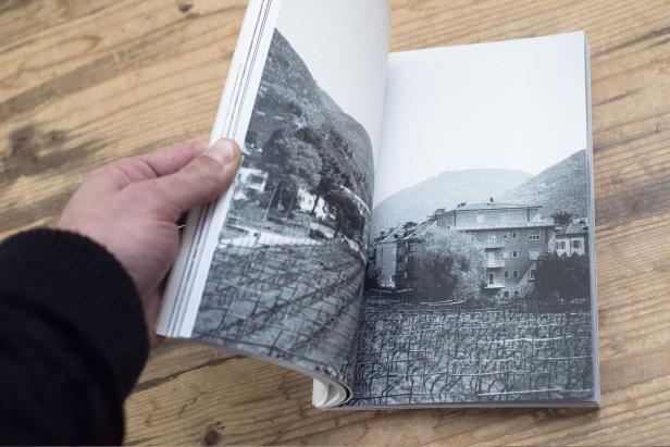 Eine Hand blättert in einem Buch mit Schwarzweißfotografien von Weinbergen und Häusern.