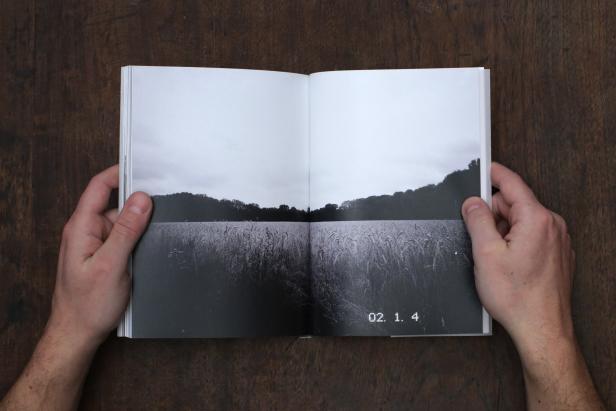 Ein aufgeschlagenes Buch zeigt eine Schwarzweißfotografie eines Feldes unter bewölktem Himmel.