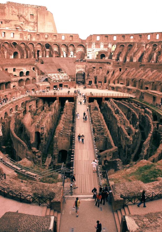 Blick in das Innere des Kolosseums in Rom mit Besuchern auf einem Steg.