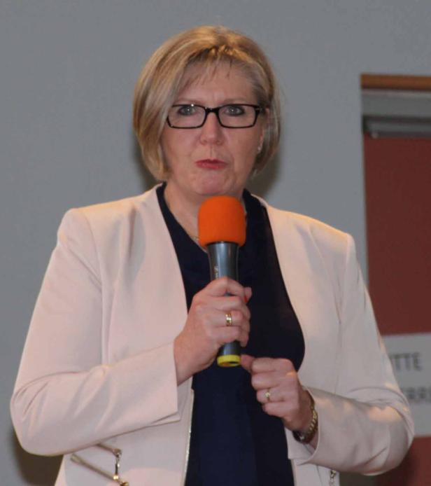 Eine Frau mit Brille spricht in ein orangefarbenes Mikrofon.