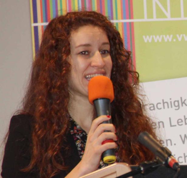 Eine Frau mit lockigem Haar spricht in ein orangefarbenes Mikrofon.