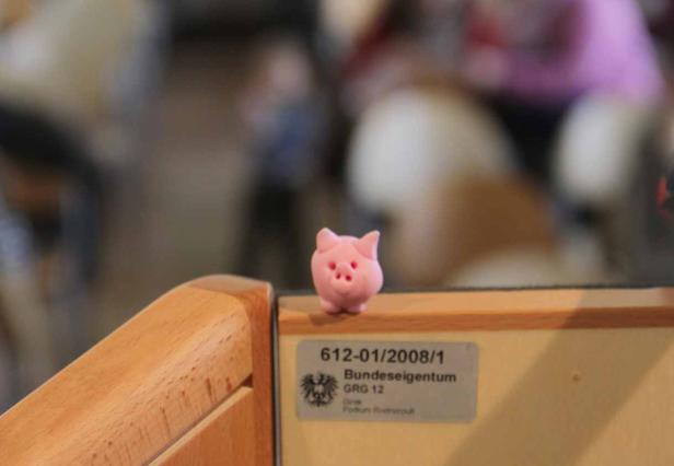 Ein kleines, rosa Schwein steht auf einem hölzernen Regal.