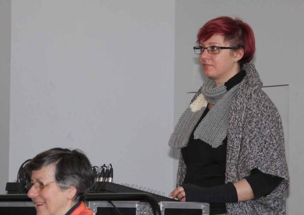 Eine Frau mit rotem Haar und Brille steht neben einem Mischpult.