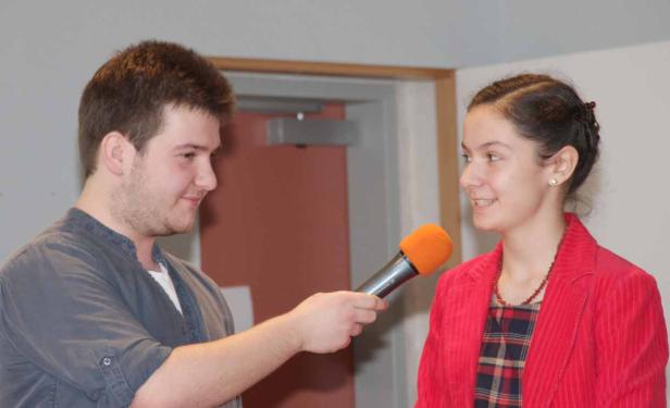 Ein junger Mann interviewt eine junge Frau mit einem orangefarbenen Mikrofon.