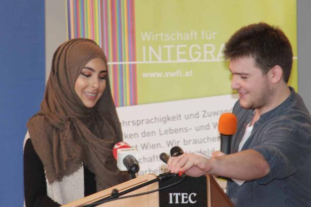 Eine Frau mit Hijab und ein Mann stehen an einem Rednerpult mit Mikrofonen.