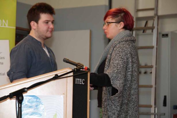 Eine Frau mit roten Haaren spricht an einem Rednerpult mit einem Mann.