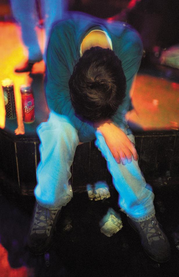 Ein Mann sitzt mit gesenktem Kopf und Geldscheinen auf dem Boden in einer Bar.