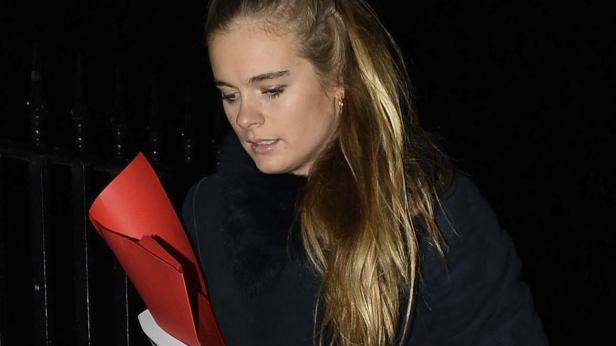 Eine Frau mit blonden Haaren hält eine rote Mappe in der Hand.