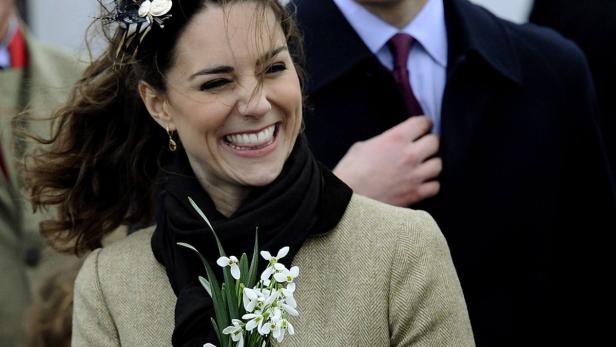 Kate Middleton lächelt und hält einen Strauß Schneeglöckchen.