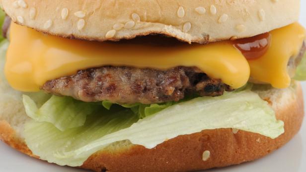 Nahaufnahme eines Cheeseburgers mit Salat, Käse und Ketchup.