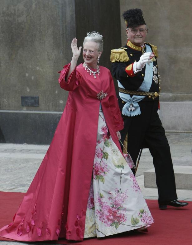 Königin Margrethe II. von Dänemark winkt in einem roten Mantel und einem blumigen Kleid.