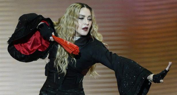 Madonna tritt in einem schwarzen Kimono und mit einem roten Fächer auf einer Bühne auf.