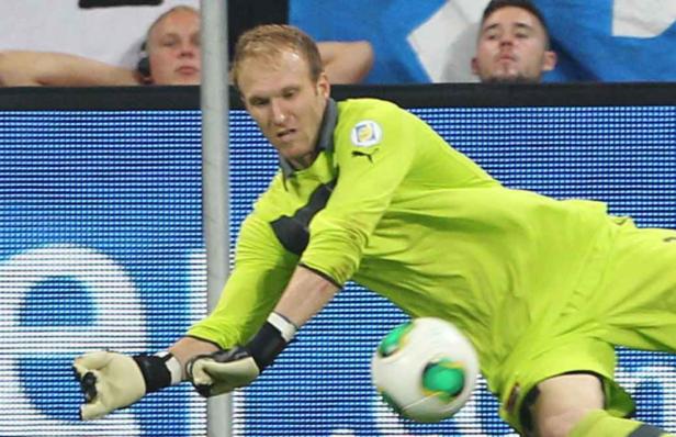 Ein Torwart in grüner Sportkleidung hechtet nach einem Fußball.