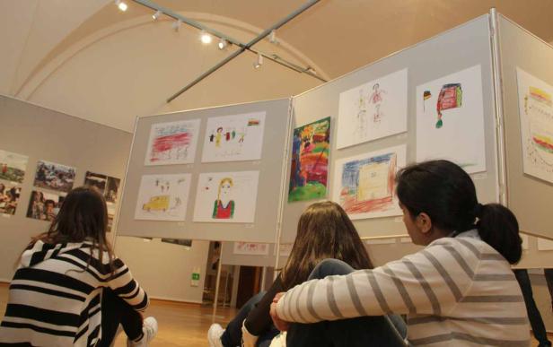 Zwei Mädchen betrachten eine Ausstellung mit Kinderzeichnungen.