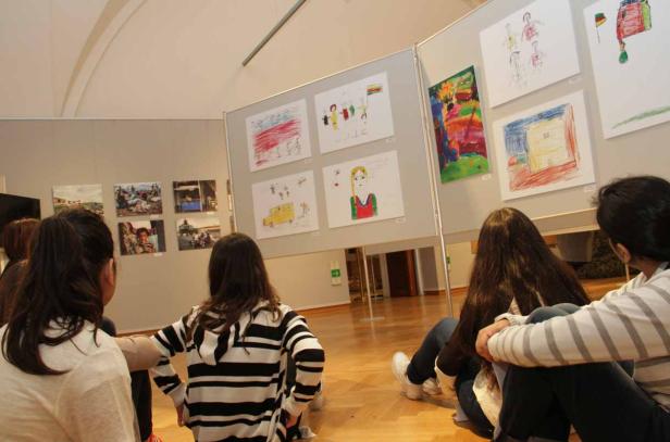 Kinder betrachten eine Ausstellung mit Kinderzeichnungen.