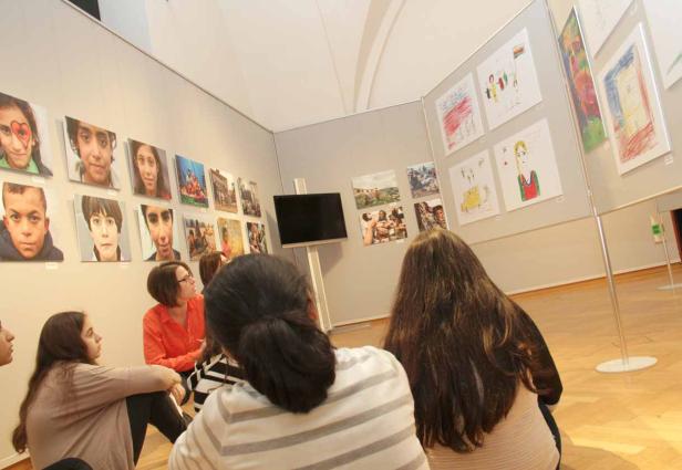 Eine Gruppe von Personen betrachtet eine Ausstellung mit Fotos und Kinderzeichnungen.