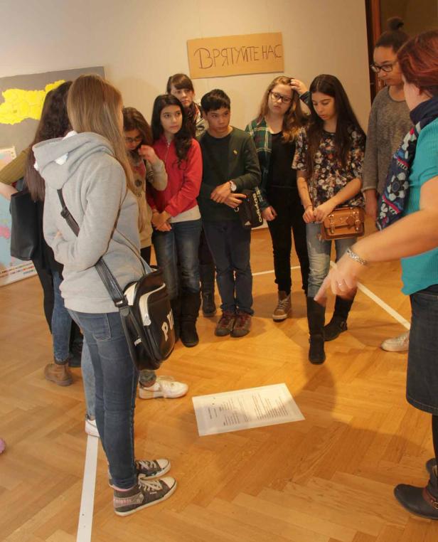 Eine Gruppe von Schülern steht um ein Blatt Papier auf dem Boden.