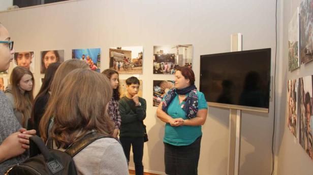 Eine Frau spricht vor einer Gruppe von Jugendlichen in einer Kunstausstellung.